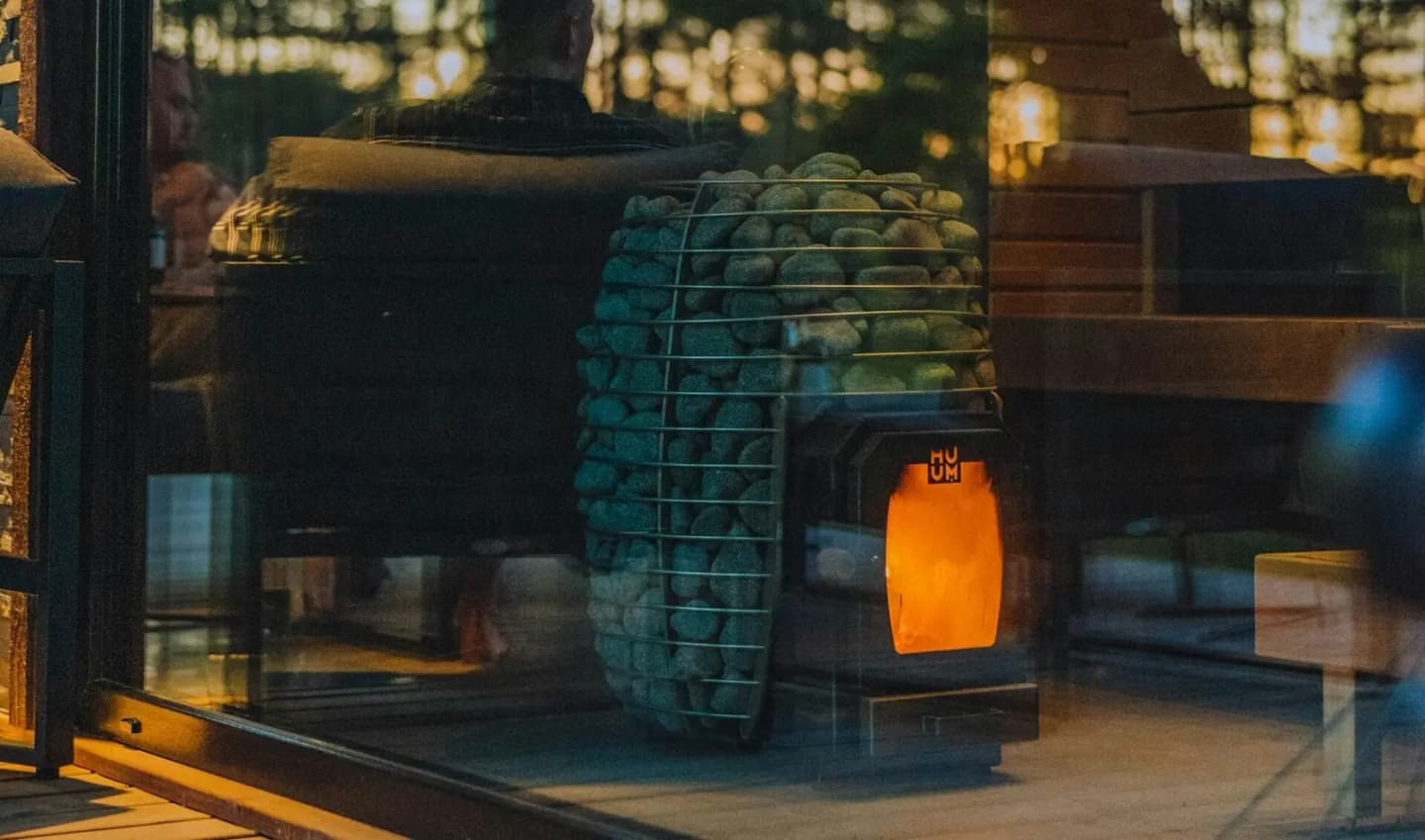 Glowing wood-fired sauna heater seen through a cabin window at dusk