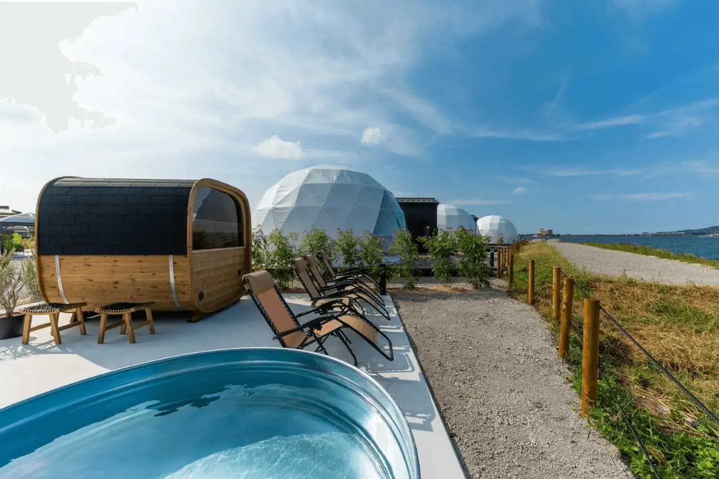 Sauna cabin beside a bright blue pool and sunbeds with the sea behind
